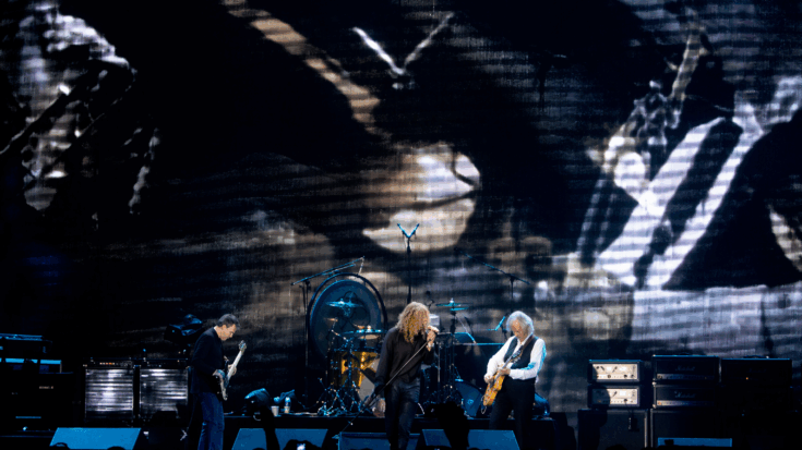 Led Zeppelin performs onstage with powerful energy, backed by a large screen displaying dramatic visuals behind them.