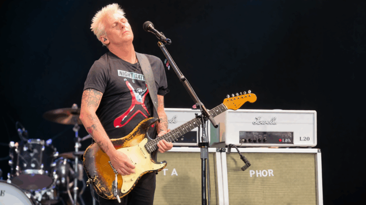 Mike McCready stands onstage with eyes closed, lost in the moment as he plays his worn electric guitar.