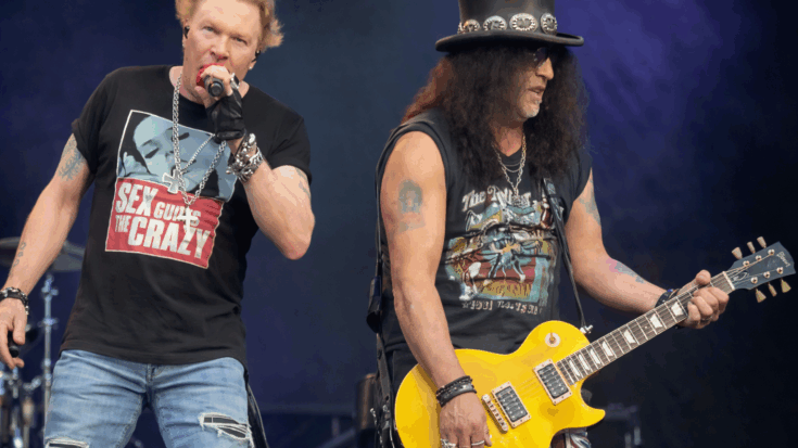 Guns N’ Roses command the stage as Axl Rose sings beside Slash, who plays a bright yellow guitar.
