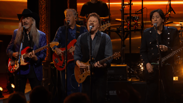 The Doobie Brothers perform together onstage, singing and playing guitars under warm golden lights.