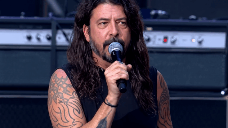 Dave Grohl speaks into the microphone onstage, showing his tattooed arms and intense expression.
