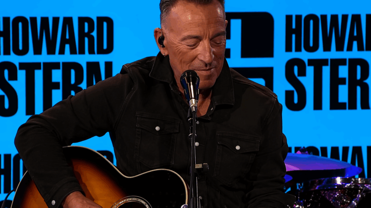 Bruce Springsteen smiles while playing an acoustic guitar during a studio performance.