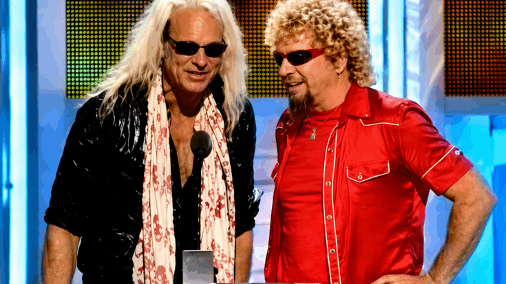 David Lee Roth and Sammy Hagar stand together at a podium wearing sunglasses, sharing a lively moment onstage.