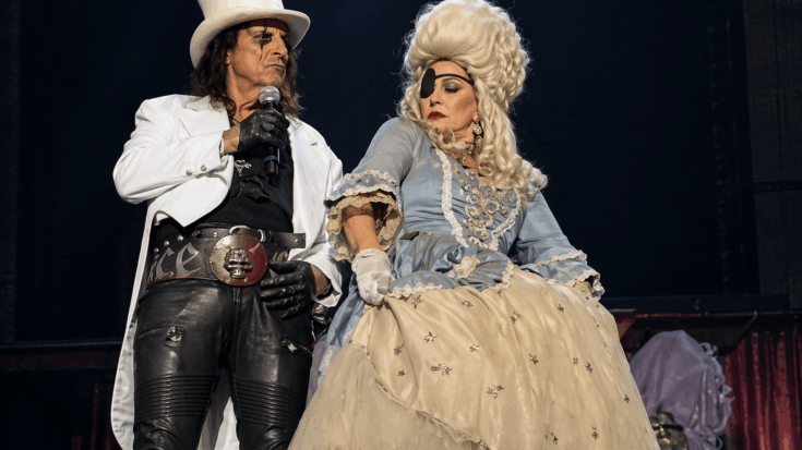 Alice Cooper and Sheryl Cooper strike a theatrical stage pose in elaborate costume under softer concert lighting.