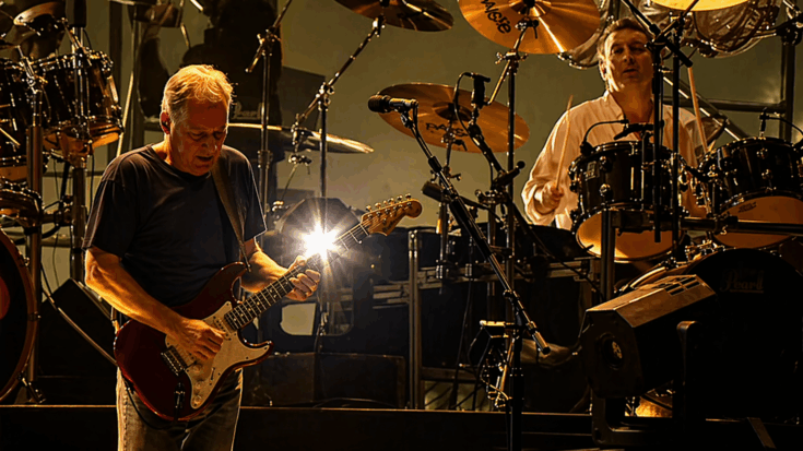 David Gilmour and the Pink Floyd members perform onstage in a dramatic glow of warm golden lights.
