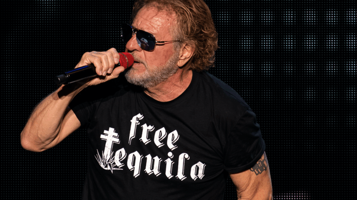 Sammy Hagar sings into a red microphone onstage, wearing sunglasses and a bold black “Free Tequila” shirt.