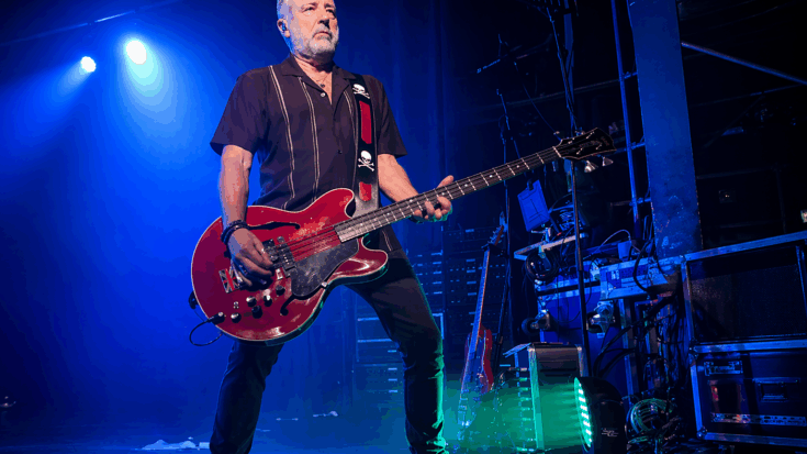 Peter Hook stands onstage under blue lights while playing a red bass guitar.