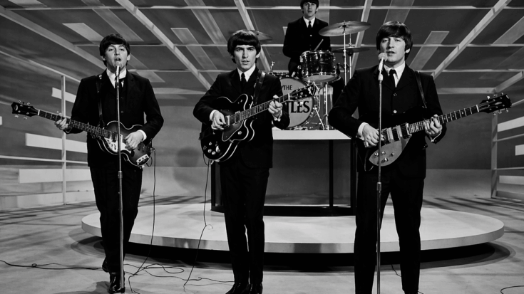 The Beatles perform together on a minimalist studio stage in a classic black-and-white television shot.