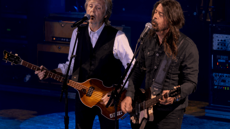 Dave Grohl and Paul McCartney sing side by side onstage while playing their guitars.