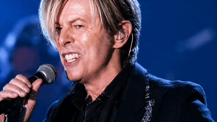 David Bowie sings into a microphone under bright blue stage lights.