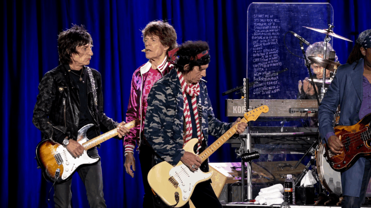The Rolling Stones perform onstage, with Keith Richards holding a cream Fender Stratocaster-style electric guitar.