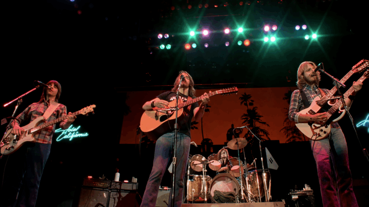 The Eagles perform live onstage under colorful lights, delivering a classic concert moment with guitars in hand.