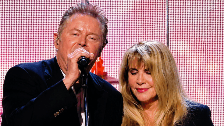 Stevie Nicks stands beside Don Henley as he sings into the microphone during a warm live duet performance.