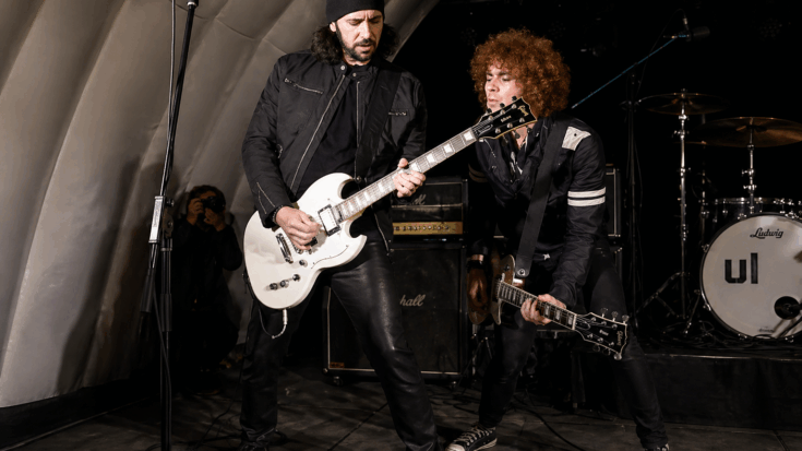 Bruce Kulick performs onstage with another guitarist, playing a white Gibson SG-style electric guitar.