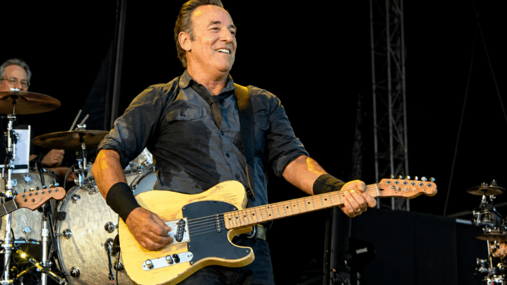 Bruce Springsteen smiles onstage while playing a worn yellow Telecaster-style electric guitar.