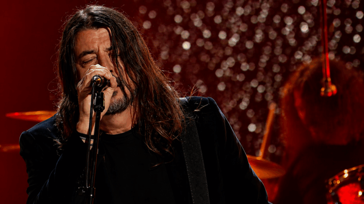 Dave Grohl sings with his eyes closed under deep red stage lights, giving the performance an emotional feel.