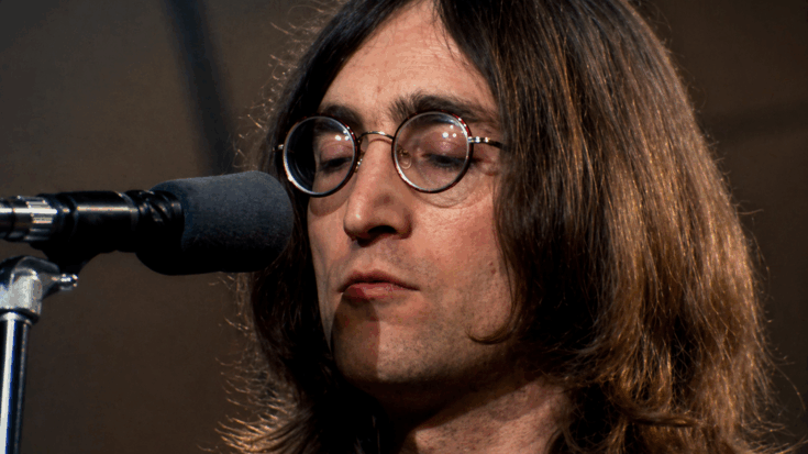 John Lennon stands calmly at the microphone, eyes closed behind round glasses as he sings with quiet intensity.