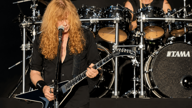 Dave Mustaine performs at the microphone while playing a black Flying V-style electric guitar.