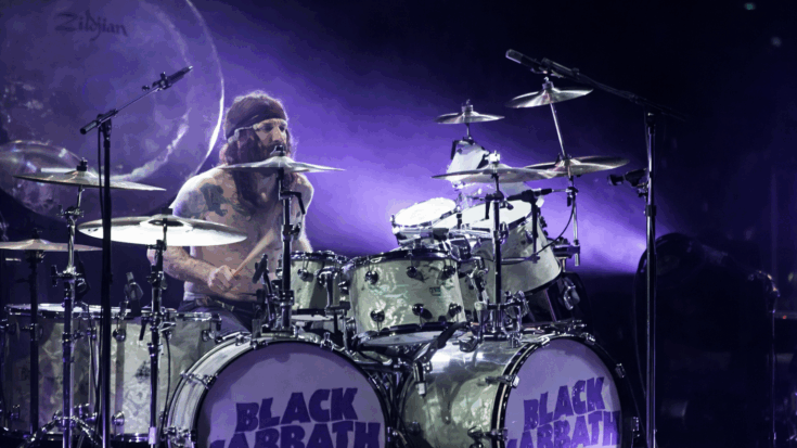 Tommy Clufetos powers through an intense drum performance under purple stage lights behind a Black Sabbath kit.