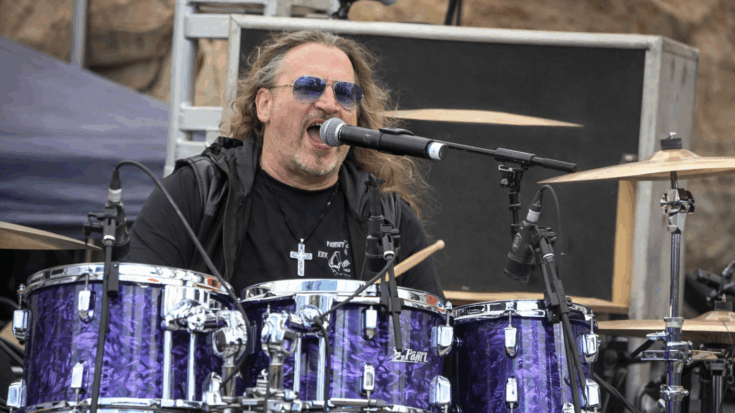 Eric Singer sings behind a purple drum kit, delivering an energetic live performance.