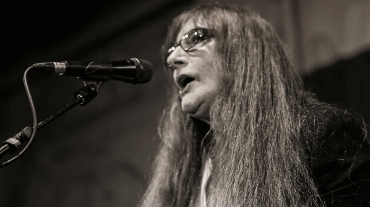Beverley Martyn sings passionately into a microphone under warm stage lighting.