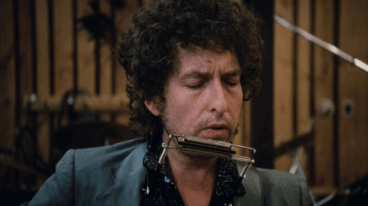 Bob Dylan plays the harmonica with his eyes closed while performing in a recording studio or on stage.
