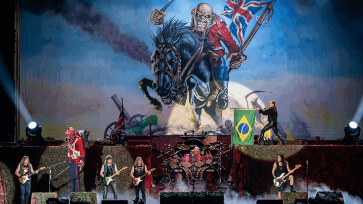 Iron Maiden performs on a grand stage dominated by a colossal, roaring mascot on a warhorse and complex pyrotechnics, featuring all six members in an energetic display.