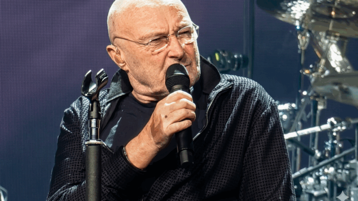 Phil Collins is shown on stage, gripping a microphone and singing with a focused, slightly intense expression while seated in front of a drum kit.
