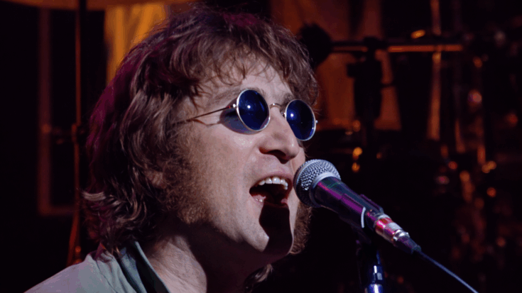 John Lennon is captured mid-performance, singing into a microphone while wearing his signature round sunglasses.