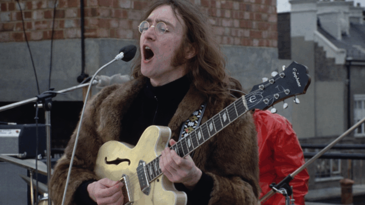 John Lennon sings passionately while playing his guitar during a rooftop performance.