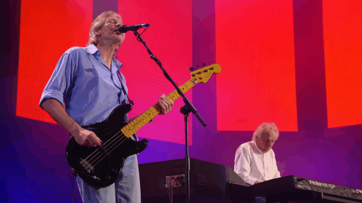 Roger Waters plays a black Fender Precision Bass while Jon Carin performs on keyboards under vivid red stage lights.