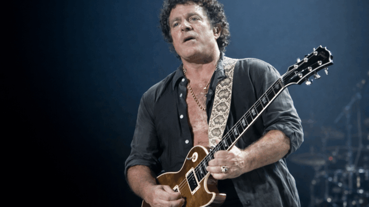 Neal Schon plays his Les Paul guitar onstage, focused under cool blue concert lighting.