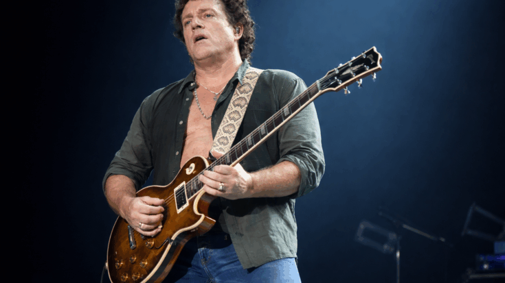 Neal Schon plays a sunburst Les Paul onstage with intense focus under bright concert lighting.