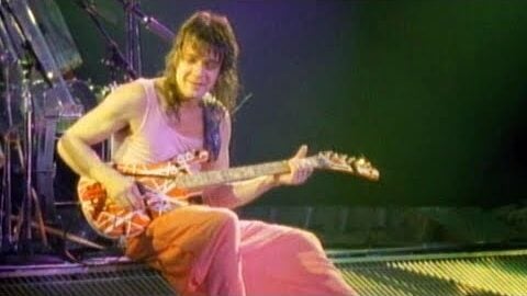 Eddie van halen sitting on stage with his iconic guitar.